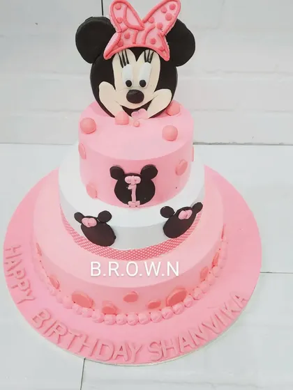 A grand three-tier Minnie Mouse cake. The pink and white design is decorated with Minnie silhouettes and polka dots, topped with a large, handcrafted Minnie figure.