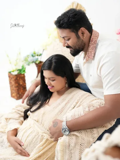 A tender moment between a couple in a cozy, boho-themed setup. The earthy tones and soft fabrics create a warm and intimate environment for their maternity shoot.