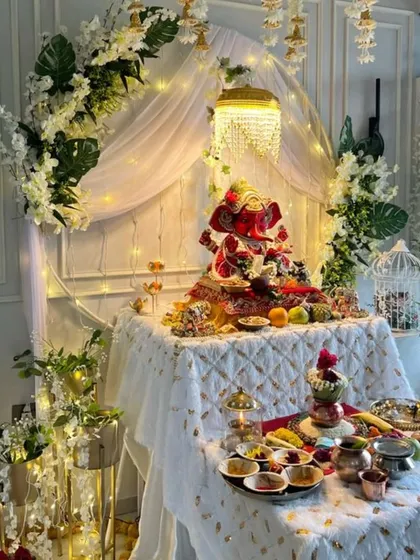 An example of pure elegance. This all-white Ganpati setup features a beautiful arch, a mini chandelier, and delicate floral arrangements, creating a sophisticated and serene atmosphere.