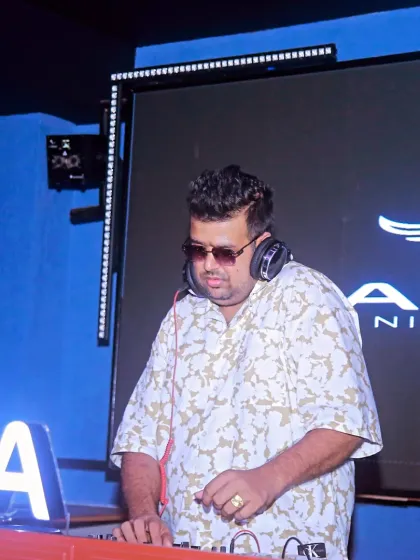 At the decks at Aura Night Club, surrounded by the signature blue lighting. I make sure every beat is perfect for the Saturday night crowd.