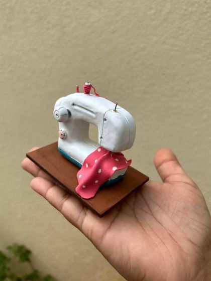 Holding the miniature sewing machine to show its small scale. It's a perfect desk accessory or keepsake for anyone who loves to sew.