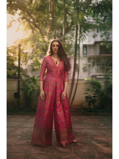 A full-length shot of the pink brocade jumpsuit, showing its flattering wide-leg silhouette in a beautiful outdoor setting.