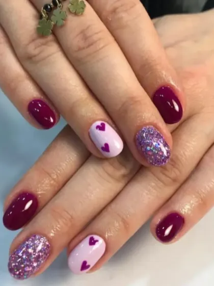 A cute and playful design combining deep magenta, sparkling purple glitter, and a lilac accent nail with tiny hearts.