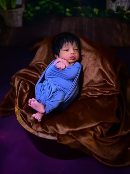 A simple and sweet newborn photo. The baby is comfortably swaddled in a blue wrap, resting on a soft brown blanket, highlighting their delicate features.