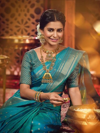 This campaign image for a jeweler showcases a classic Maharashtrian bridal look. The model wears a beautiful teal blue silk saree, accessorized with stunning temple jewelry, including a long necklace and matching earrings.