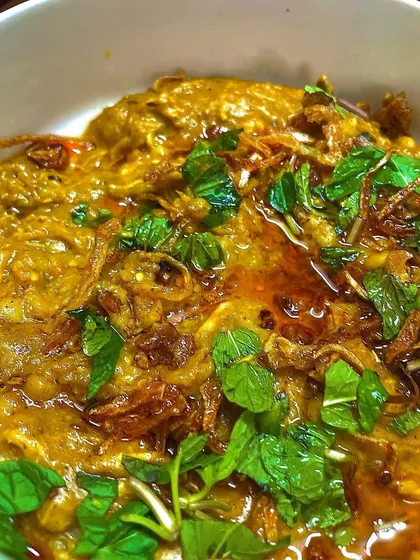 A bowl of rich and hearty Daleem (Haleem), slow-cooked with meat, lentils, and wheat, and garnished with fresh mint and fried onions.