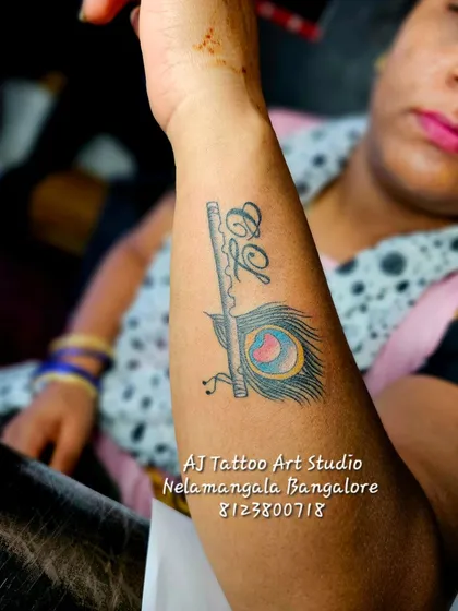 A creative design combining a flute, peacock feather, and initials on the forearm.