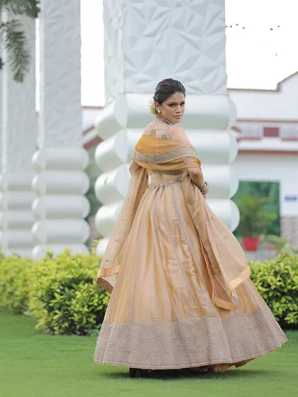 A model looking over her shoulder while wearing the gold lehenga, her hair adorned with a white rose.