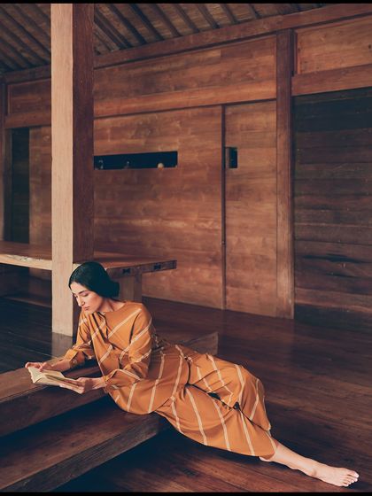 Reading in a quiet corner of the villa. This lifestyle shot helps create a narrative of a peaceful retreat, making the collection feel aspirable and wearable.