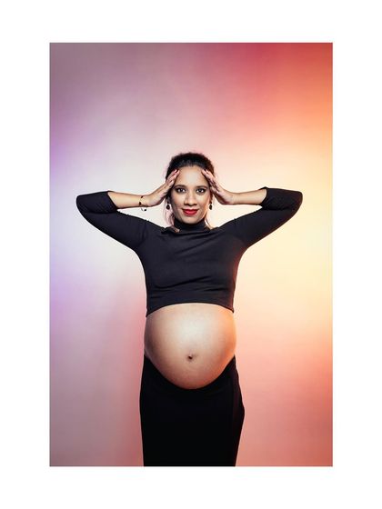 A powerful and fashionable studio shot of an expectant mother posing with her hands on her head. The creative lighting and confident pose celebrate the strength and beauty of the female form during pregnancy.