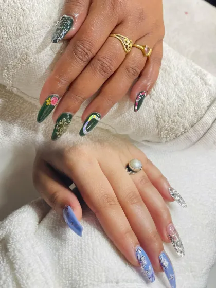 Our students learn to create a wide range of nail extension styles. This image displays two distinct sets of professional nail art, one with dark green polish and intricate floral and gold foil details, and another with a soft periwinkle blue and sparkling silver accents.