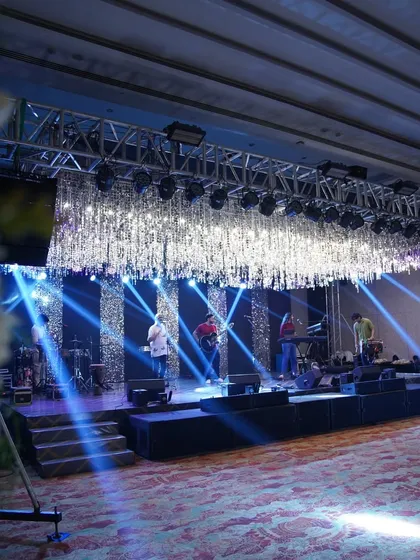 A behind-the-scenes look at a band setting up on a glamorous stage, featuring a ceiling of silver tassels and dramatic blue lighting.