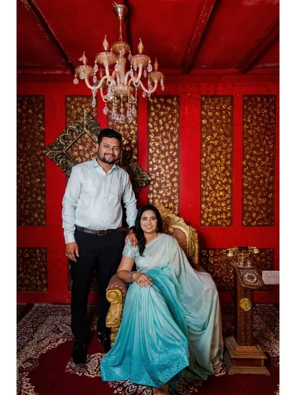 A grand, royal-themed pre-wedding portrait. The ornate chair and rich red background give this photo a luxurious and timeless feel.