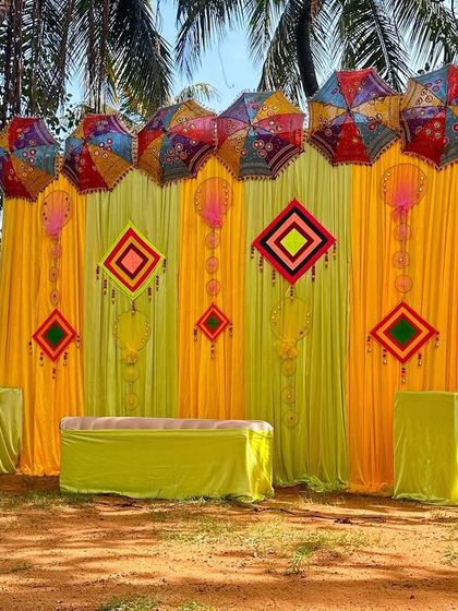 A bright and sunny Haldi or Mehendi setup with yellow drapes and colorful umbrellas, perfect for an outdoor event.