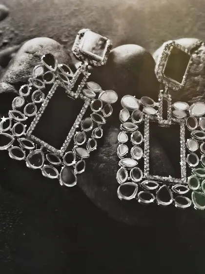 A black and white shot of statement earrings on a textured stone surface, with a soft light flare adding a touch of glamour and artistry.