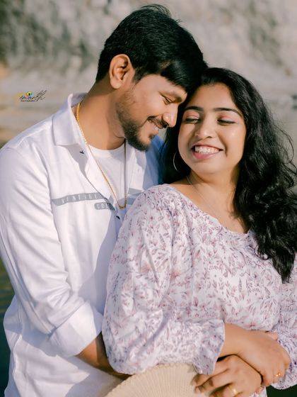 A bright, happy close-up of a couple embracing by the water. Their genuine smiles are the focus of this warm and sunny portrait.
