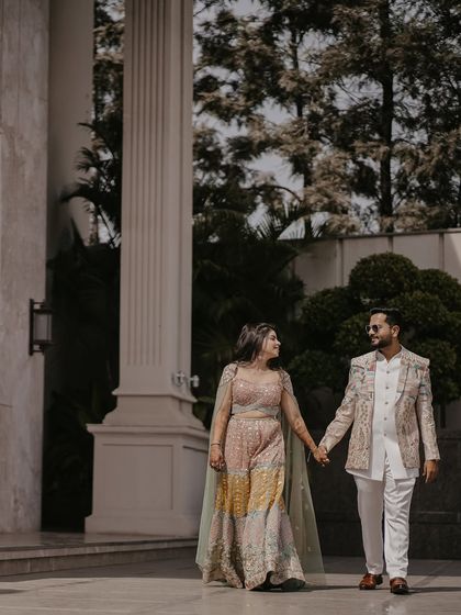 The couple walks hand-in-hand past towering modern pillars. This candid shot captures their regal style and connection in a grand, contemporary architectural space.