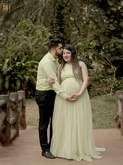 A tender kiss on the forehead during an outdoor session. The couple is coordinated in soft green tones, blending beautifully with the park's foliage.
