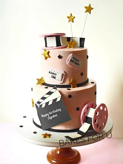 A two-tier movie-themed cake perfect for a film buff. The design includes a clapperboard, film reels, and movie tickets, all made from edible materials.