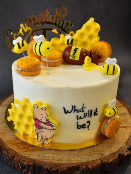 "What will it bee?" This adorable Winnie the Pooh and honeybee-themed cake was created for a baby shower. It features cute fondant bees, honeycomb details, and macarons, all on a delicious chocolate cake.