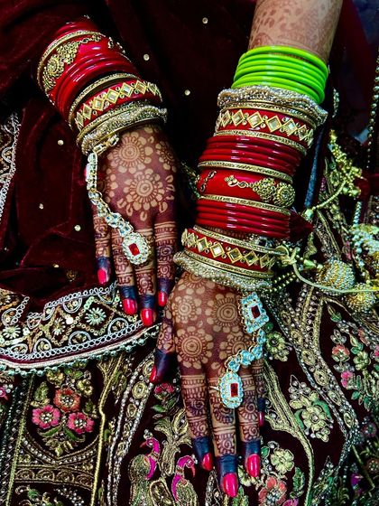 A still photo of the bride's hands, capturing the deep red stain of the mehndi against her velvet lehenga.