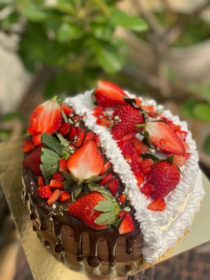 A beautiful example of our half and half cake, featuring fresh strawberries. One side is rich chocolate with a chocolate drip, and the other is light vanilla cream.