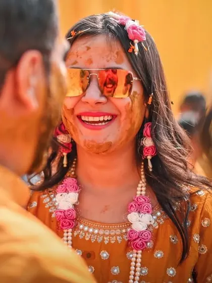 A beautiful close-up of the bride, smiling through the turmeric paste. We focus on capturing the bride's joy and radiance, complete with her stylish sunglasses and floral jewelry.