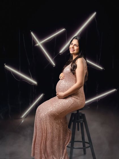 A modern and glamorous solo portrait, with the mom-to-be in a sequin gown posing against a backdrop of dramatic neon lights.