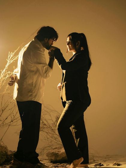 A chivalrous and romantic gesture. The father-to-be kisses his partner's hand in a beautifully lit, artistic studio setting, creating a timeless and elegant portrait.