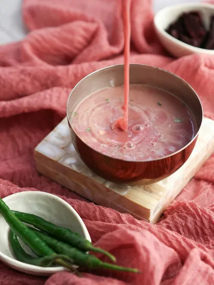 The vibrant pink of Sol Kadhi being poured, creating ripples in the bowl. This captures the refreshing quality of the coastal drink.
