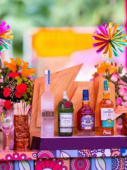 A bar that matches the party's vibe. For our "Rangeela Rajasthan" theme, we decorated the bar with colorful prints, floral arrangements, and fun pinwheels, making it a festive spot for guests to grab a drink.