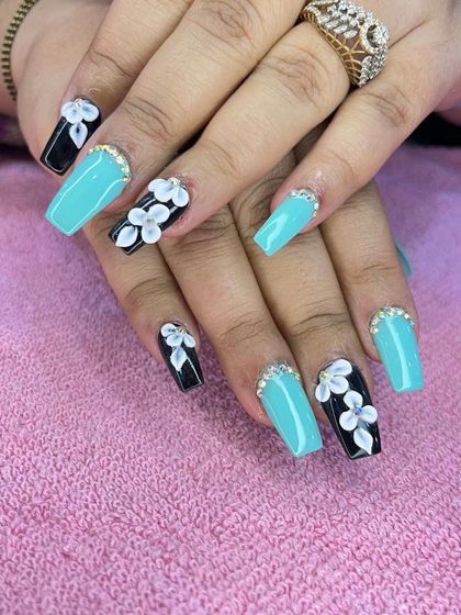 A vibrant set of coffin nails alternating between a bright turquoise and black with 3D white flowers, all finished with a crystal at the base.