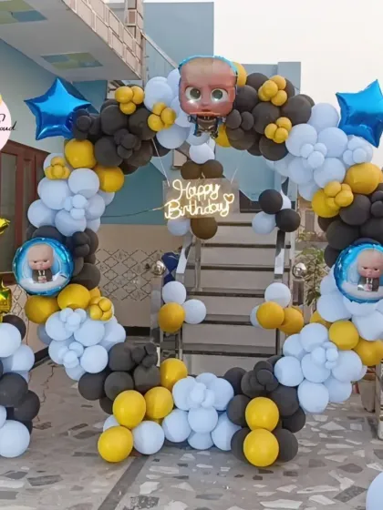 An outdoor Boss Baby themed 4th birthday party with a heart-shaped balloon arch in black, white, and yellow.