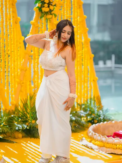 A serene look for a Haldi ceremony in a white draped outfit from The Azmat Official. The yellow marigold background provides a beautiful contrast.
