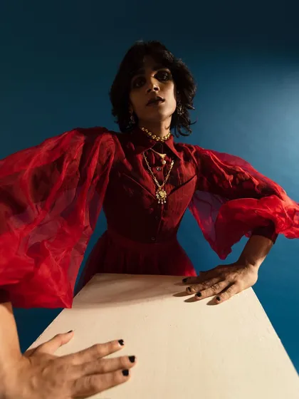 A dramatic, wide-angle shot for Amama Jewels. The pose, bold red attire, and high-contrast lighting create a powerful image that showcases the statement jewelry.