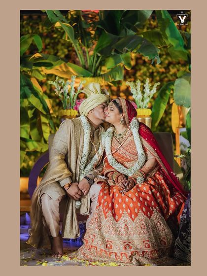 A sweet kiss on the cheek, a moment of pure affection captured during the wedding ceremony. The lush green background and their traditional attire make this a vibrant and heartwarming shot.