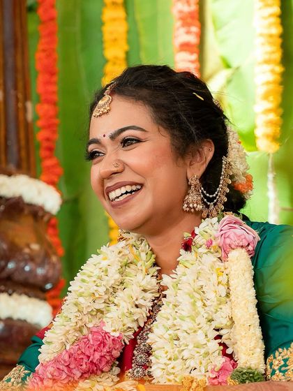 A moment of pure happiness. This candid shot captures the bride's radiant smile, enhanced by a soft glam look with gold eyeshadow and a rosy nude lip that complements her traditional temple jewellery.