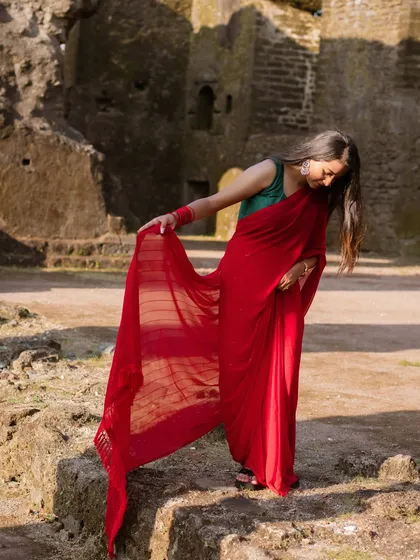 A beautiful solo portrait of the bride-to-be, showcasing the elegant drape of her red saree against the rustic texture of the fort.