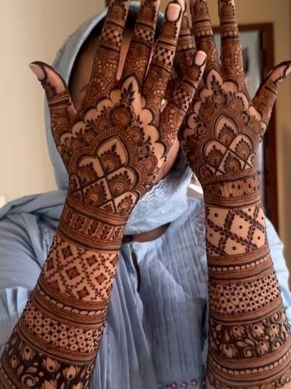 A lovely shot of a bride in a hijab showcasing her full bridal mehndi, featuring traditional domes and geometric patterns.