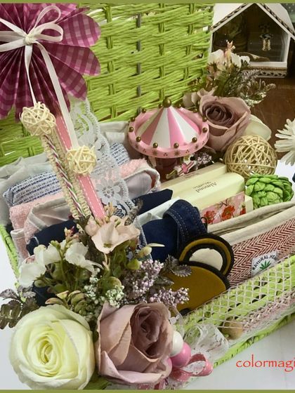 A custom baby hamper designed as a keepsake. This vibrant green woven basket is filled with a variety of textures and items, including a miniature carousel, folded baby clothes, and decorative floral elements.