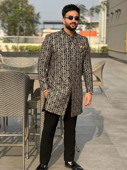 The same black and gold brocade jacket, seen from a different angle. The rich fabric and sharp tailoring create a powerful silhouette.