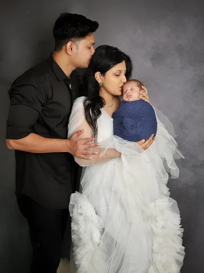A father's gentle kiss on his wife's forehead as she holds their newborn son. This is a timeless pose that beautifully captures the love and emotion of new parenthood.