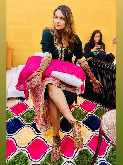 A full-length shot of the bride-to-be, relaxing after her mehndi application. You can see the coordinated designs on her hands and feet.