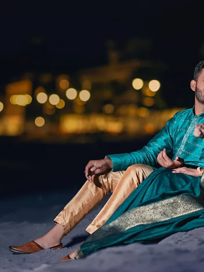 A candid conversation on the sandy ghat at night. The beautiful teal saree and the soft lighting create a rich, intimate portrait of the couple sharing a quiet moment.