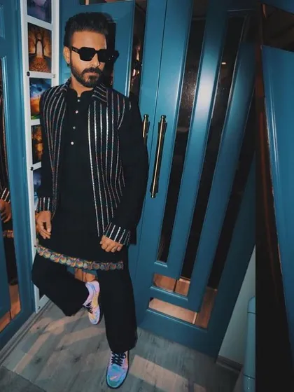 A masterpiece of modern festive wear. This black kurta is paired with a striking silver-striped bandi jacket, worn here by artist Naitik Nagda.