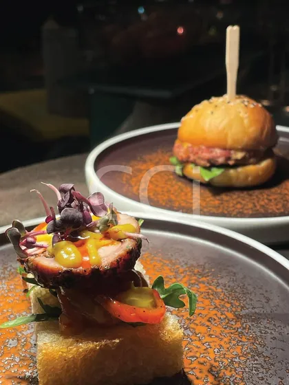 We specialize in gourmet canapés and small plates that delight the senses. This pairing shows our range, featuring a savory open-faced toast with cured meat and microgreens alongside a miniature gourmet slider, perfect for cocktail hours.