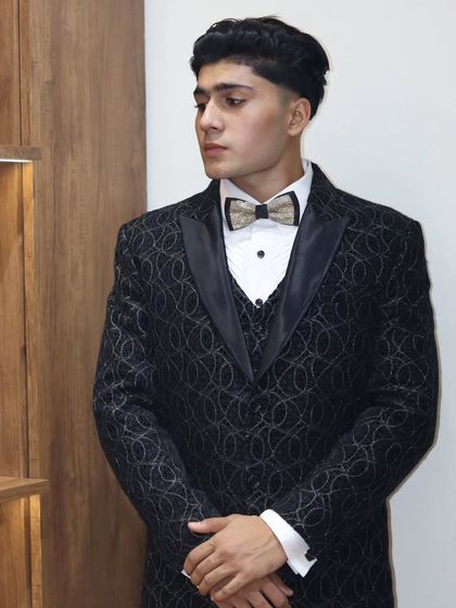 A full view of a client wearing a custom black tuxedo with a subtle circular pattern. Paired with a crisp white shirt and a statement bow tie, this look is ready for any high-profile event.