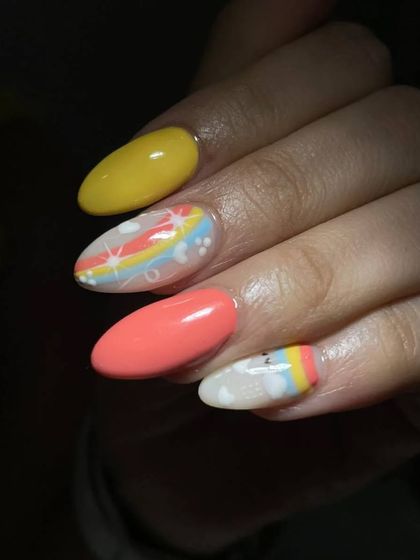 A close-up of the cute, hand-drawn rainbow and cloud nail art. The combination of coral, yellow, and pastels is so cheerful.