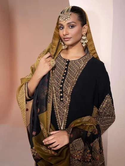 A close-up of a model in a black embroidered kurta, part of a festive campaign. The styling focuses on the intricate gold embroidery and the traditional jewelry, creating a look of classic, understated luxury.