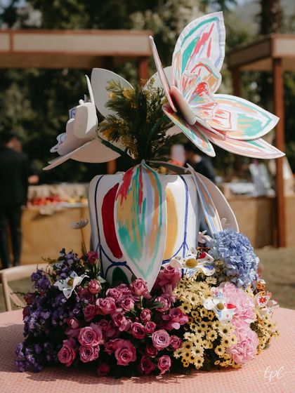 A vibrant centerpiece from the carnival-themed Mehendi, featuring colorful fresh flowers and whimsical paper butterflies.